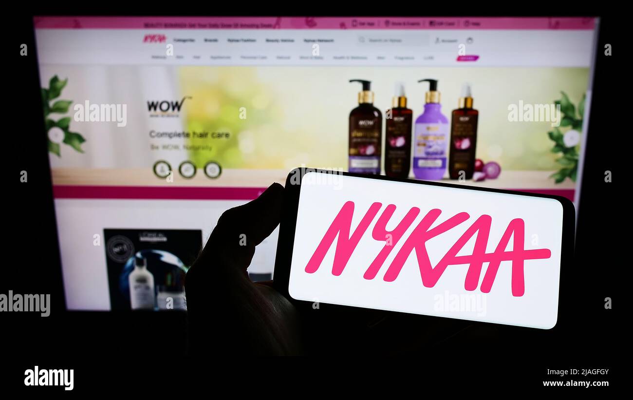 Person holding cellphone with logo of e-commerce company Nykaa E-Retail Pvt. Ltd. on screen in front of business webpage. Focus on phone display. Stock Photo