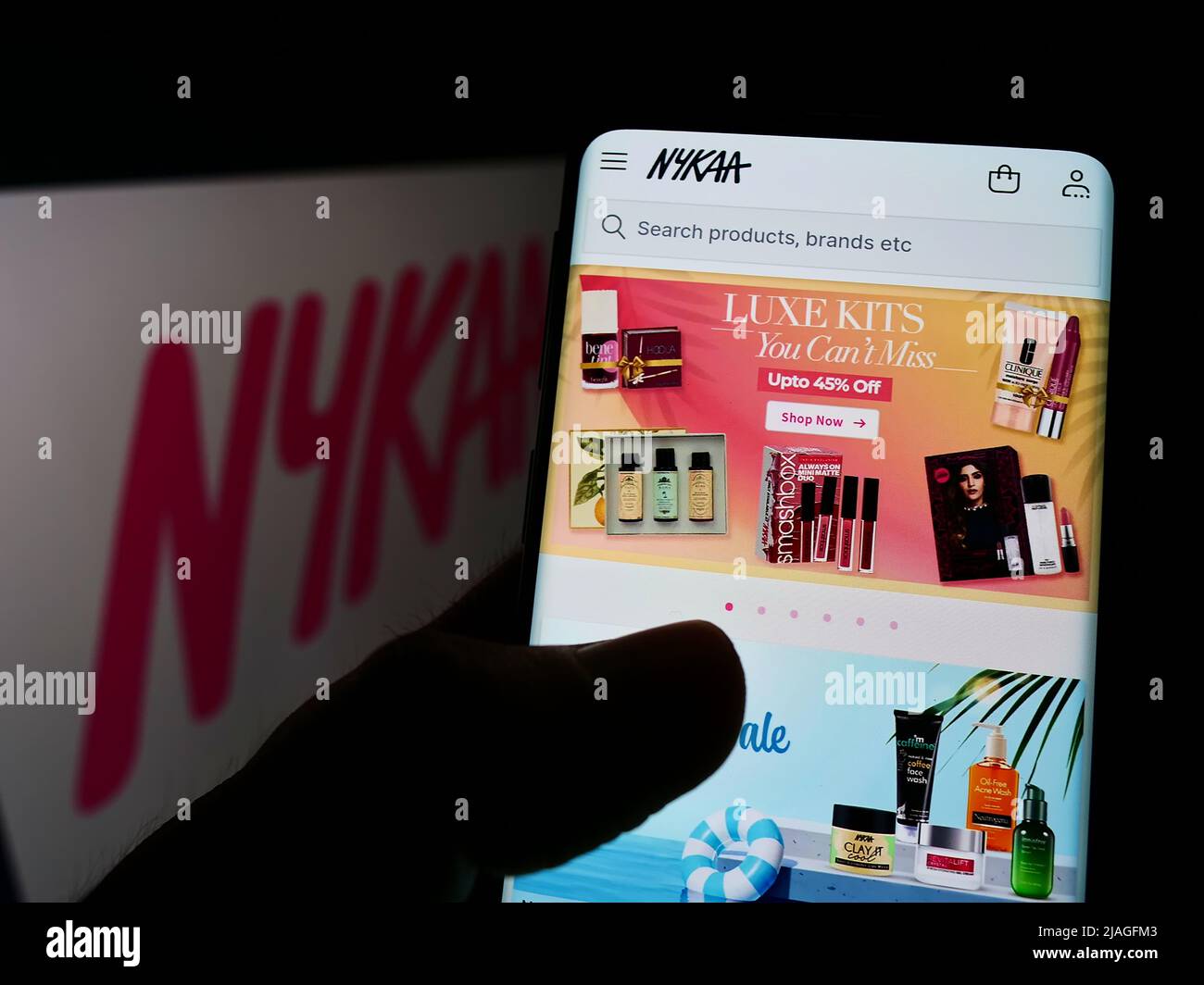 Person holding cellphone with webpage of e-commerce company Nykaa E-Retail Pvt. Ltd. on screen in front of logo. Focus on center of phone display. Stock Photo