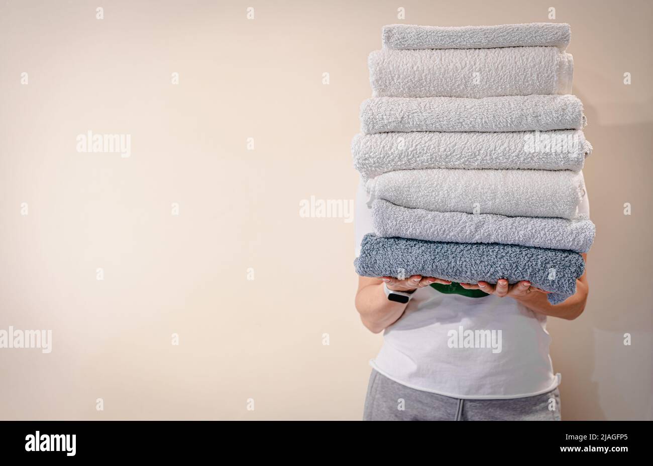 Woman holding a stack of clean white bath towels on light background ...