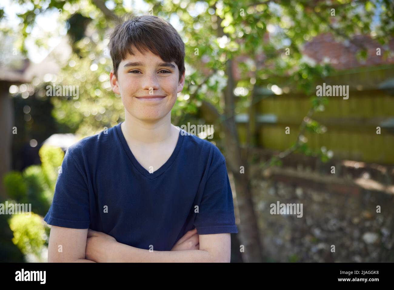 Portrait Of Smiling Teenage Boy With Crossed Arms Standing In Summer Garden At Home Stock Photo