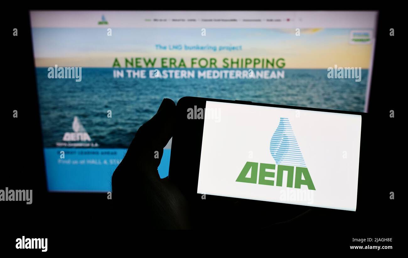 Person holding smartphone with logo of Greek energy company DEPA Commercial S.A. on screen in front of website. Focus on phone display. Stock Photo