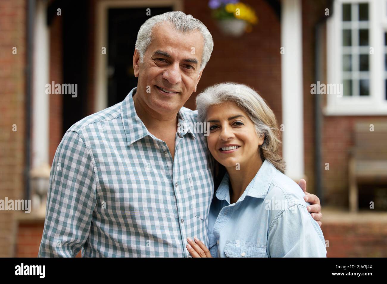 Portrait Of Mature Couple Standing In Garden In Front Of Dream Home In Countryside Stock Photo
