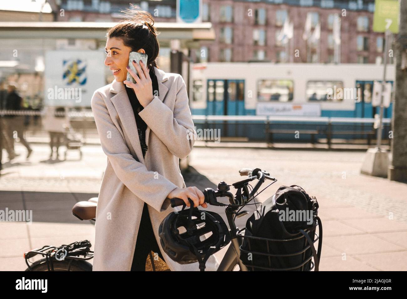 Businesswoman talking on smart phone standing with bicycle while looking back over shoulder in city Stock Photo