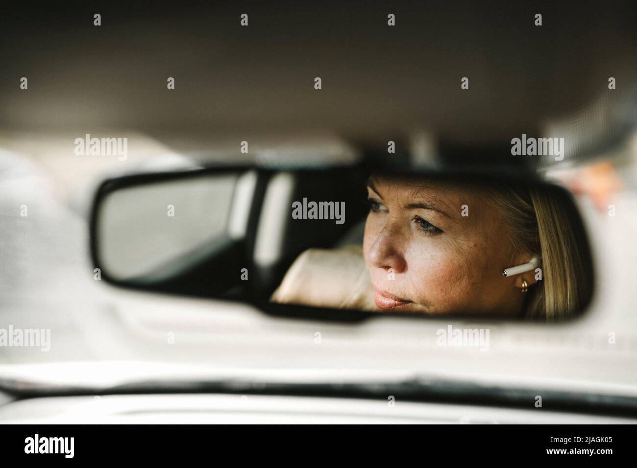 Businesswoman with in-ear headphones seen in rear-view mirror reflection of car Stock Photo
