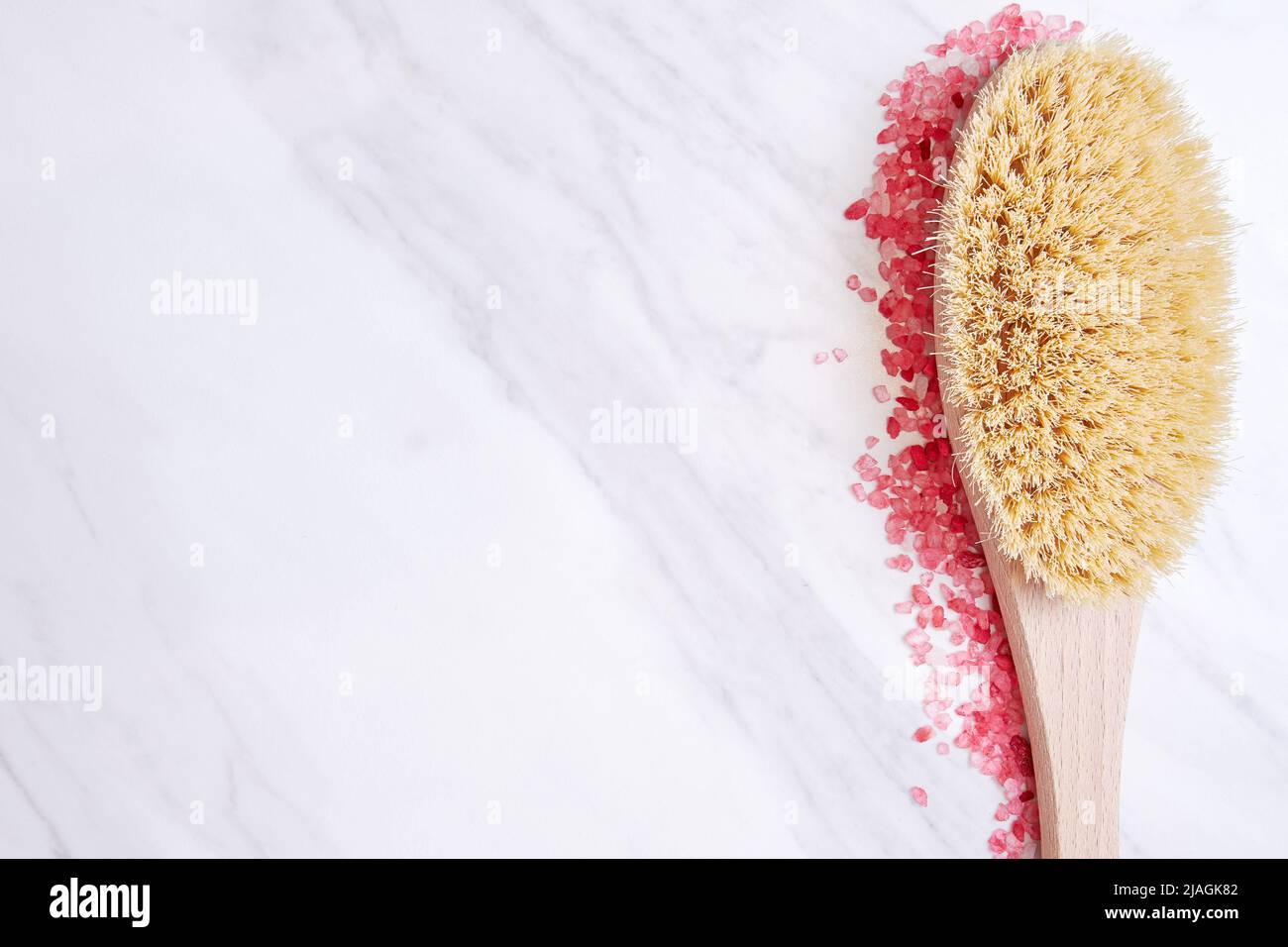 Wooden scrub brush bordered with pink bath salt grain. Relaxation therapy and body care background with a copy space Stock Photo