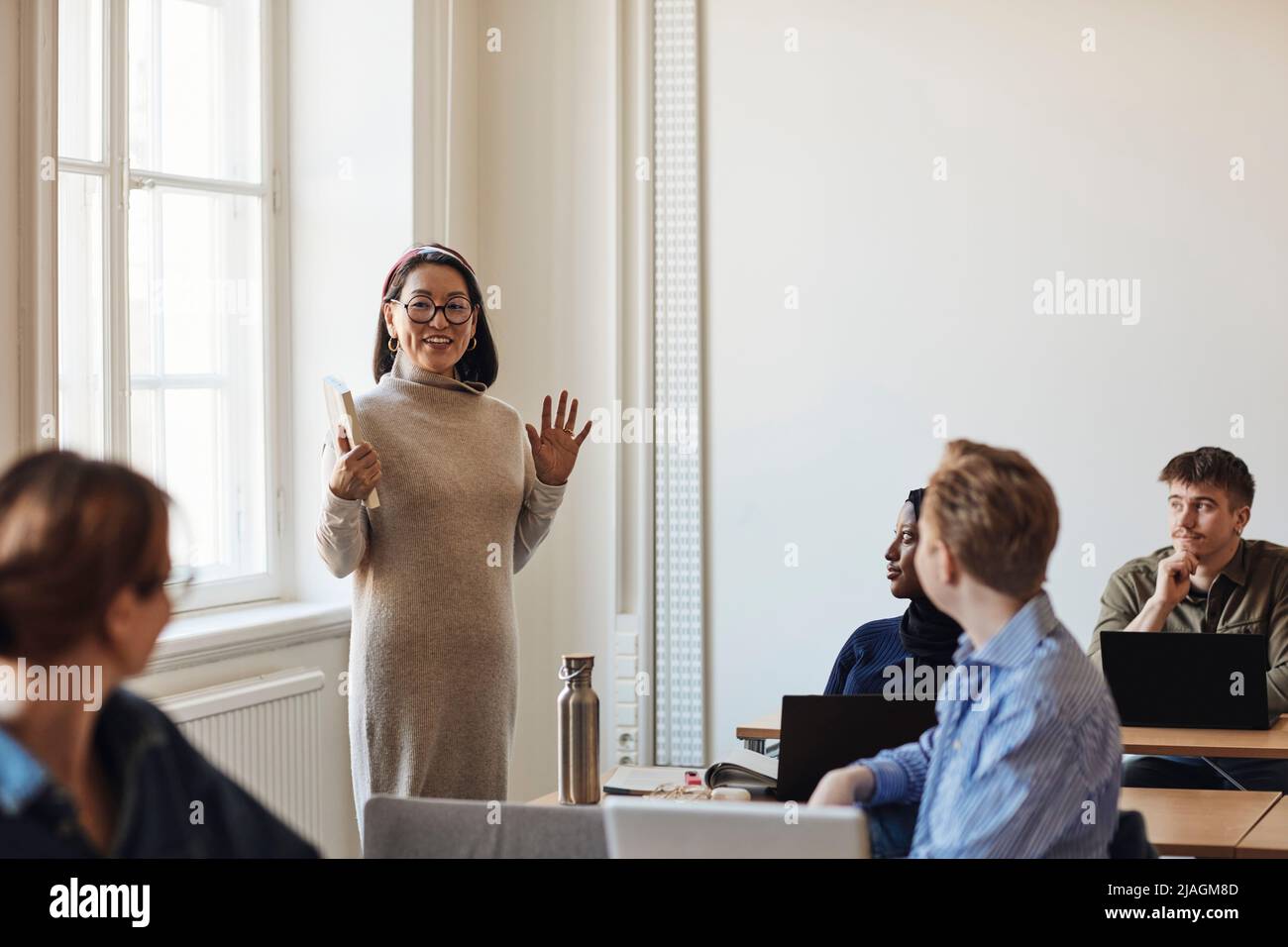 Smiling female teacher gesturing while teaching students in classroom Stock Photo