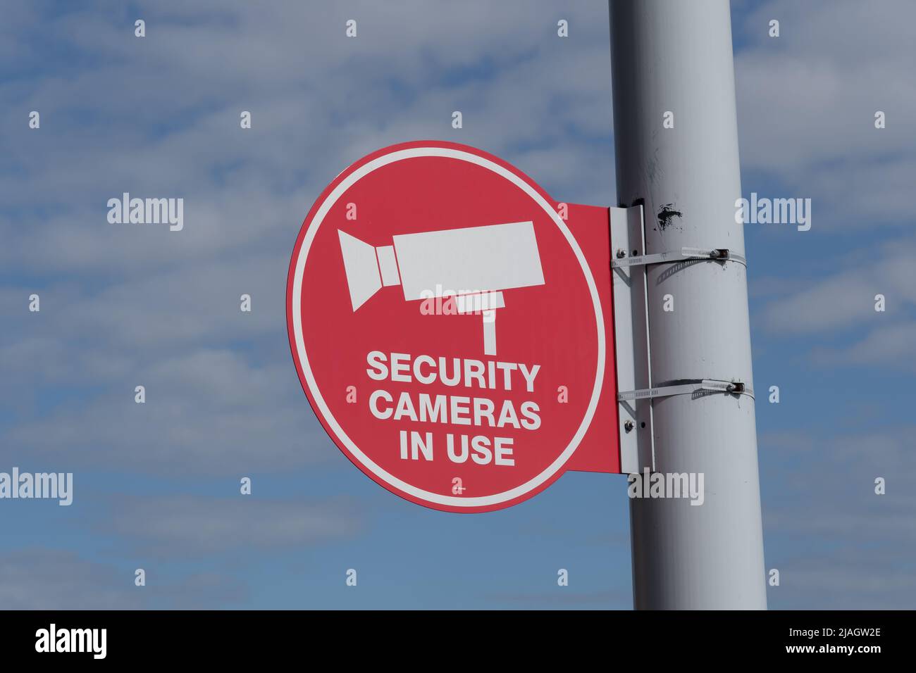 A red ‘Security Cameras in Use’ sign on the light pole with a tree and ...