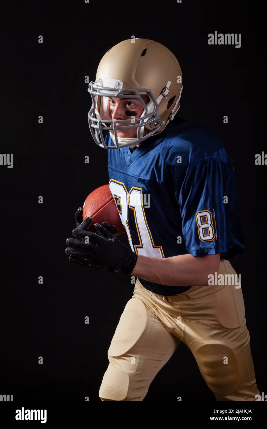 Young football player running with ball on dark background Stock Photo