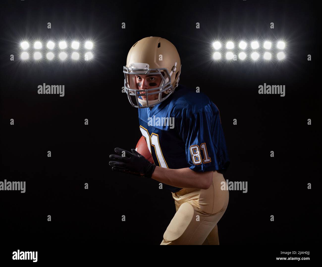 Young football player in running action on a dark background with stadium lights Stock Photo