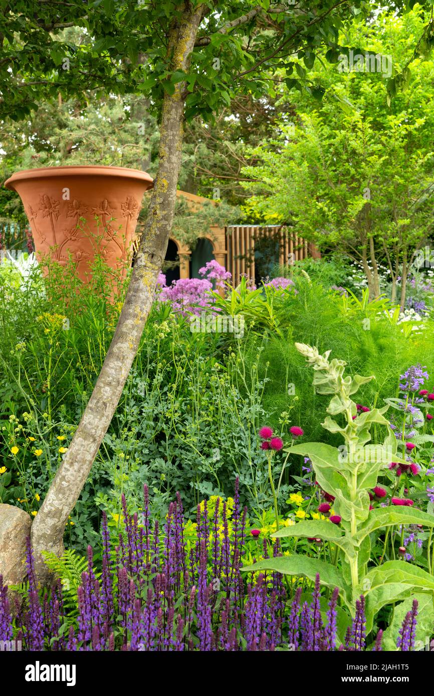 An ornamental urn decorated with a thistle pattern designed by Whichford Pottery under Carpinus betulus and surrounded by herbaceous perennials in the Stock Photo