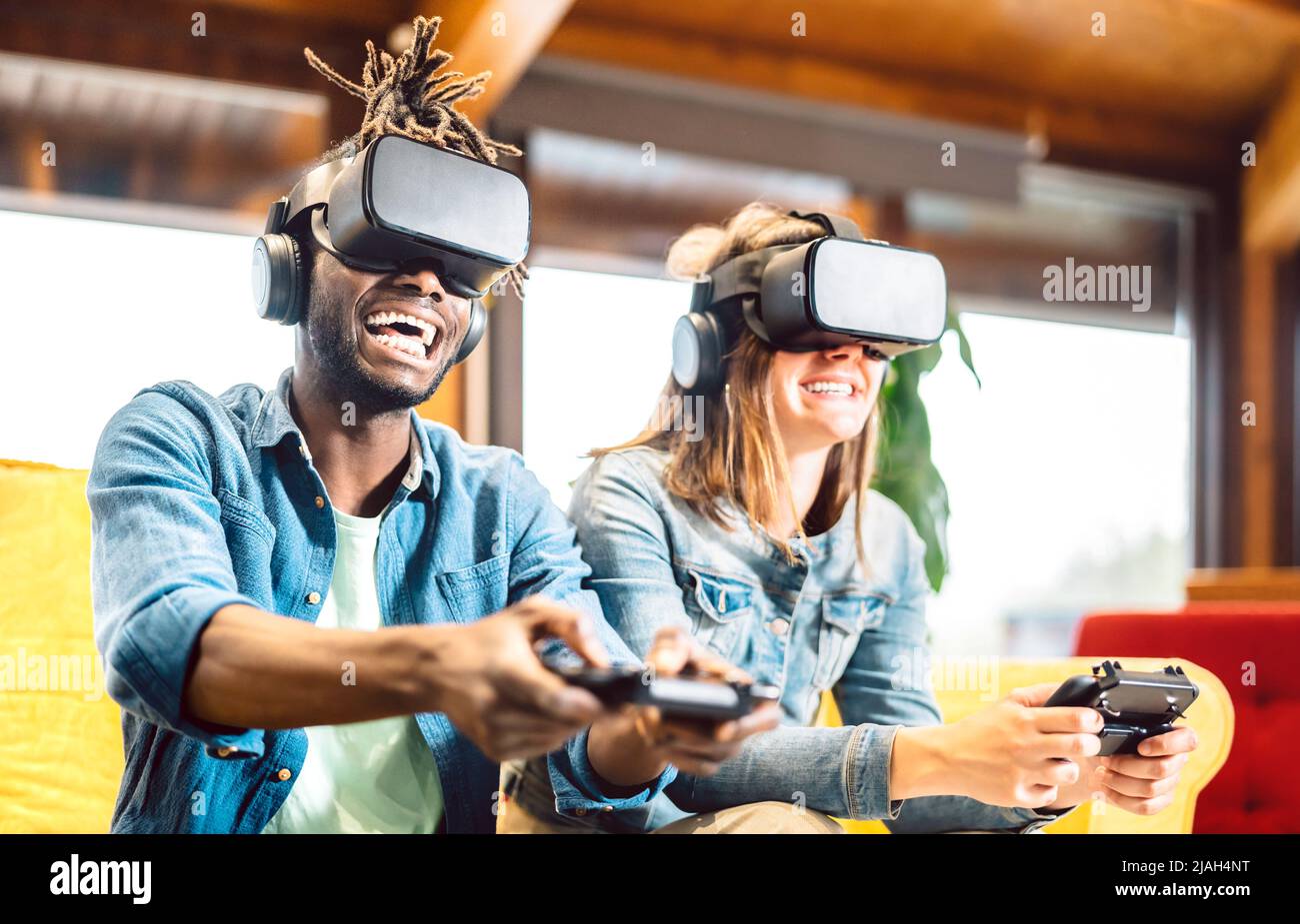 Millenial couple playing with vr glasses at home couch - Virtual reality and tech concept with enthusiastic friends having fun on headset goggles Stock Photo