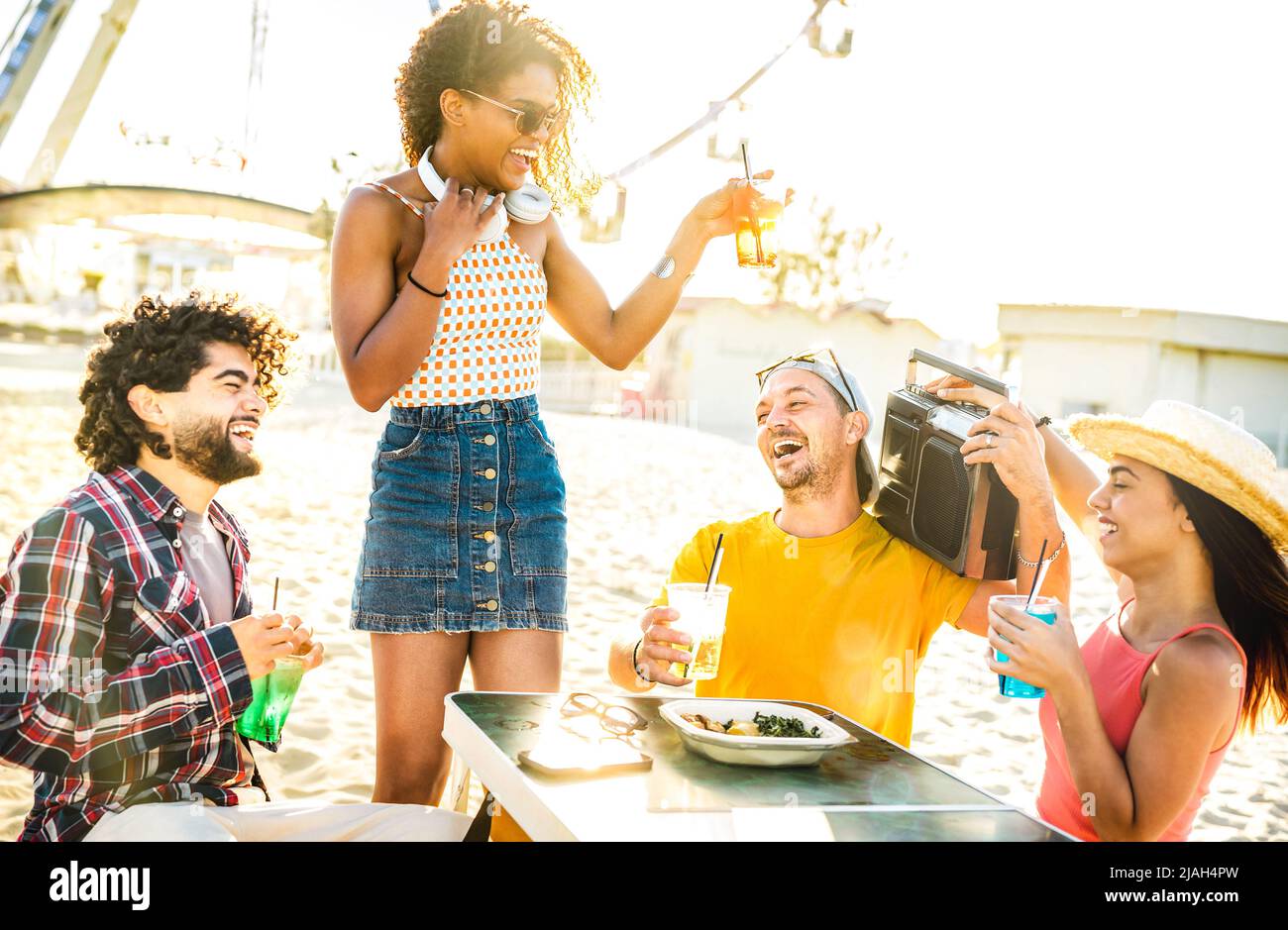 Happy men and women at sunset on vacation days - Summer life style concept with friends having fun together drinking at spring break beach festival Stock Photo