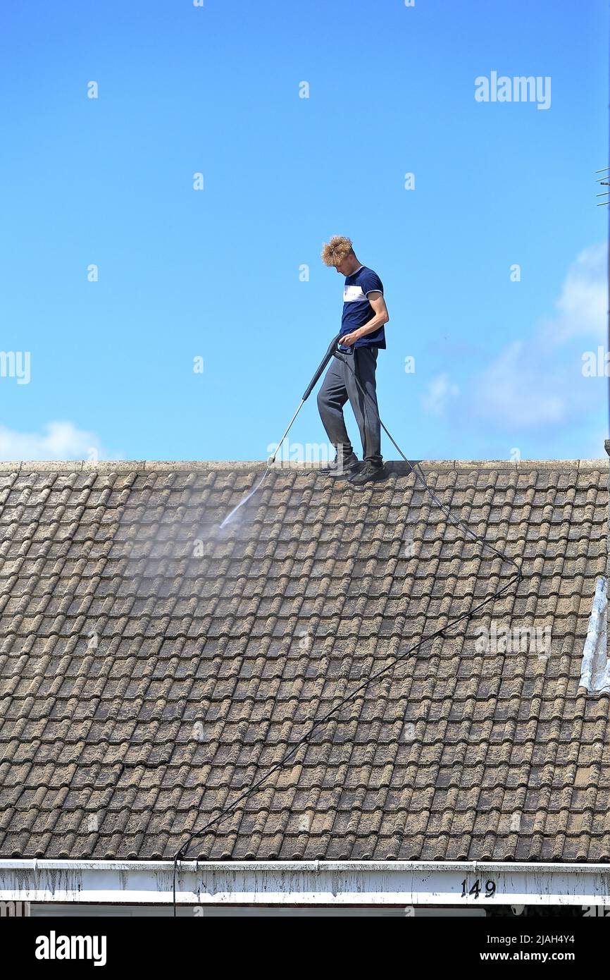 Person working at height jet washing a roof with no safety equipment or