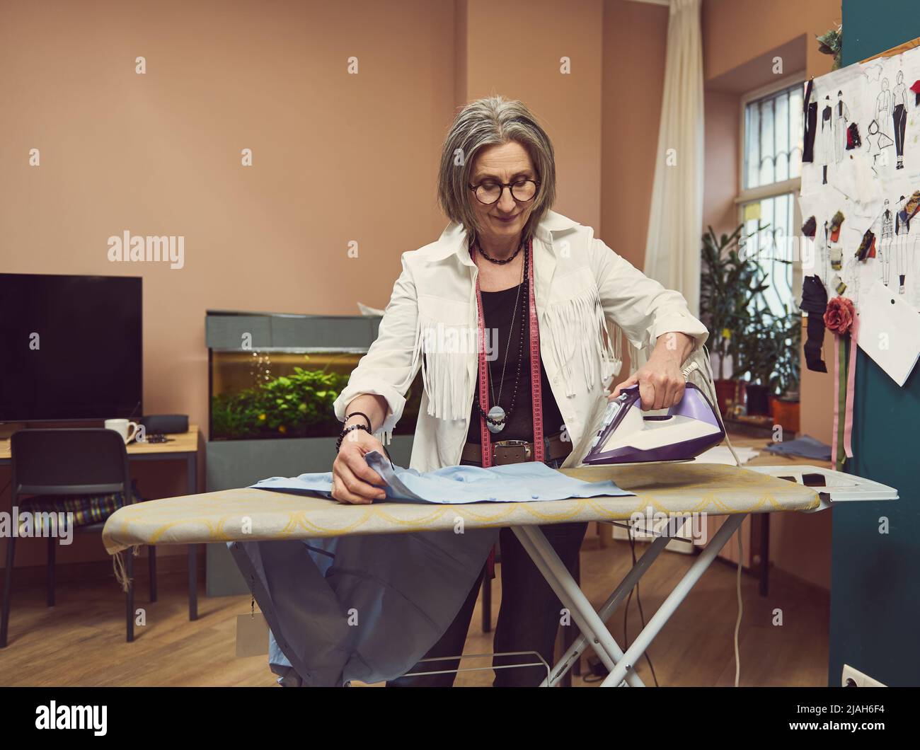 Portrait of a fashion designer tailor holding a steam iron ironing a blue shirt on an ironing