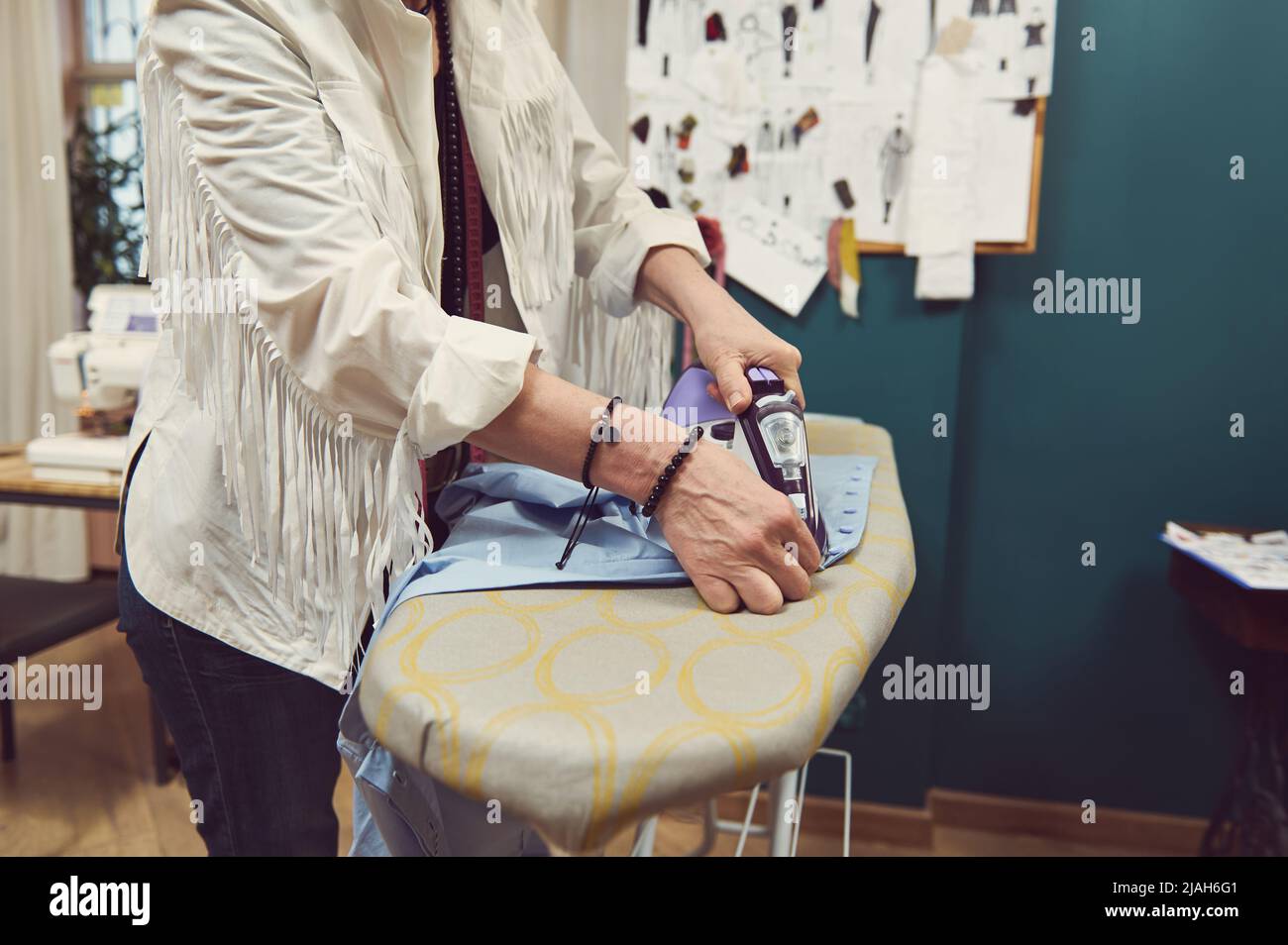 Detail of tailor's hands using steamer iron ironing clothes on ironing