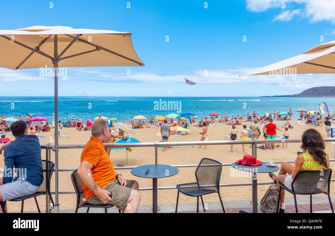Las Palmas, Gran Canaria, Canary Islands, Spain. 30th May, 2022. Tourists  look on as a parasol, lifted by a gust of wind, flies through the air on a  packed city beach in
