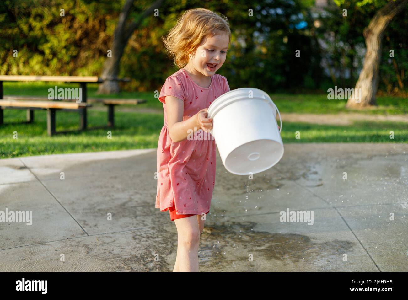 Happy smiling child playing with bucket at splash pad in park in summer