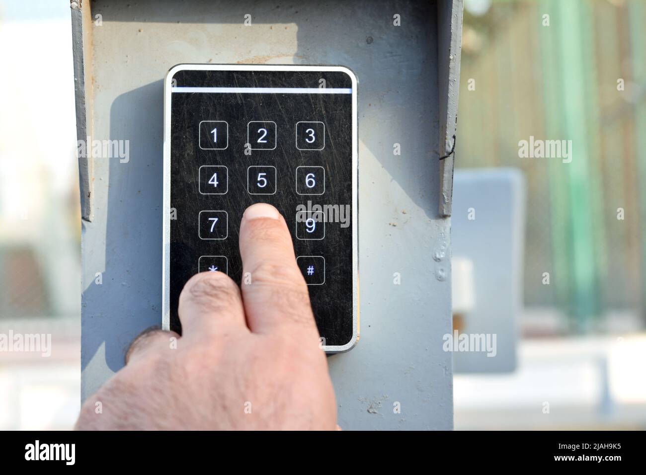 a persons hand pressing a password on a numerical keypad to lock or unlock an alarm system, opening garage gate for car entry, alarm system technical Stock Photo