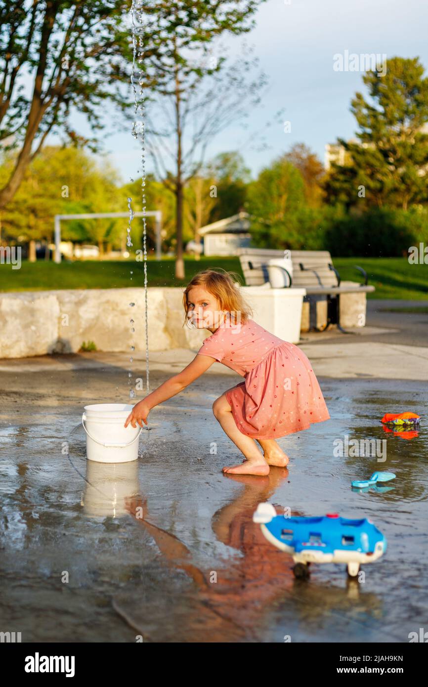 Happy child playing with toys and water in park splash pad. Girl at playground in summer barefoot Stock Photo