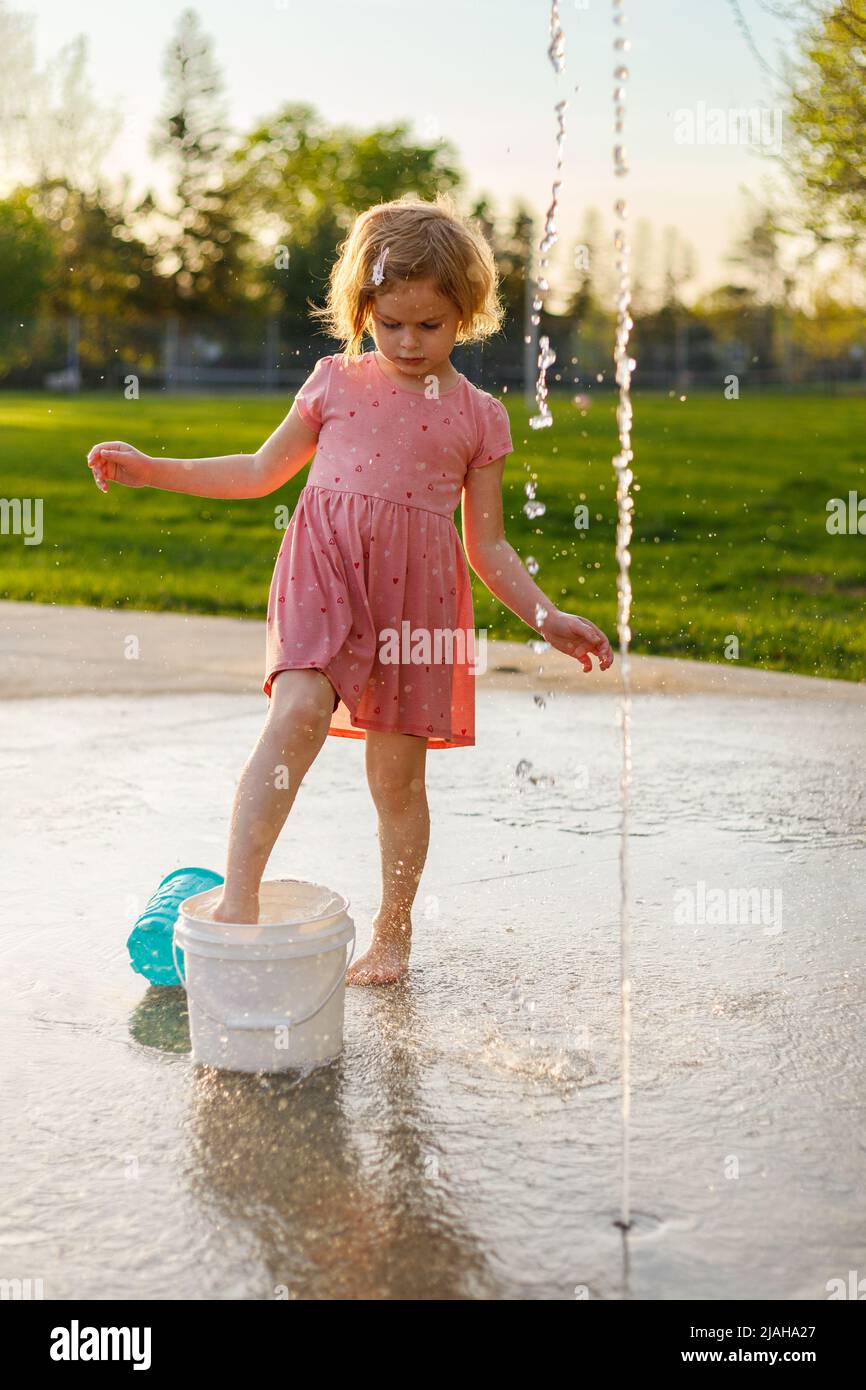 Little girl playing in park with fountains in summer Small child having fun at splash pad playground Stock Photo