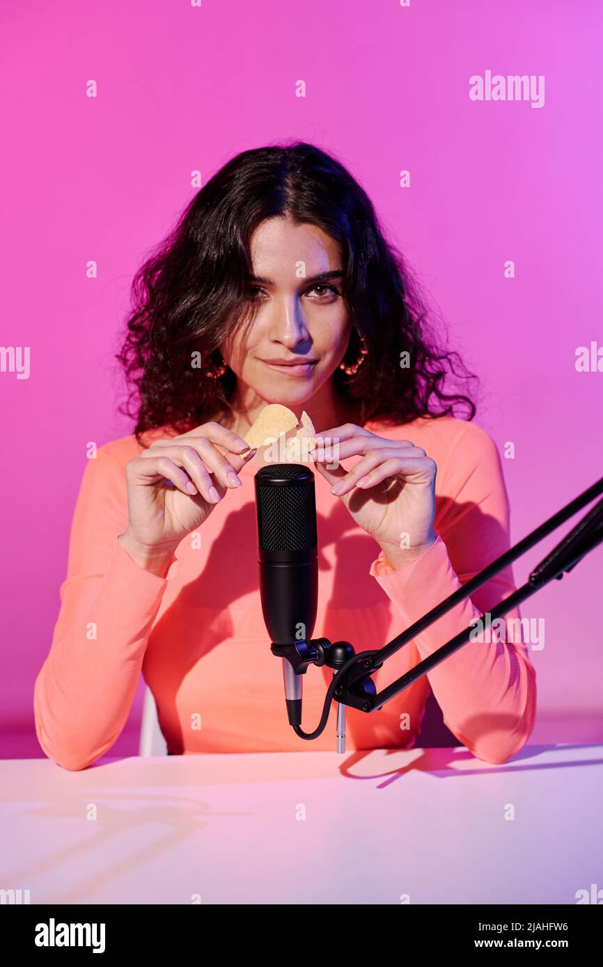 Attractive young female blogger sitting at desk in studio in pink neon