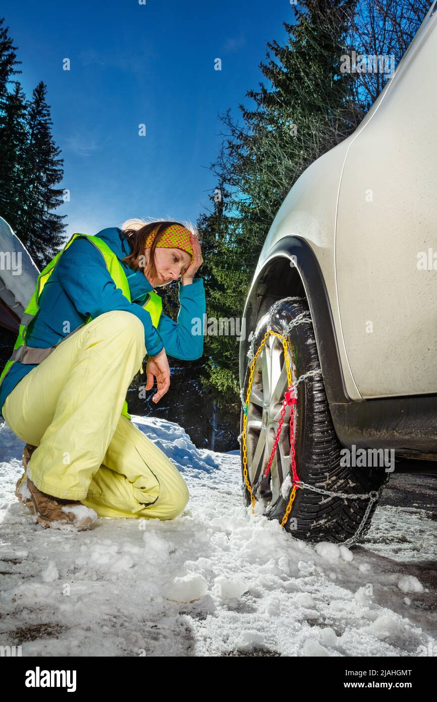 Troubled woman with confused expression putting chains on wheel Stock Photo