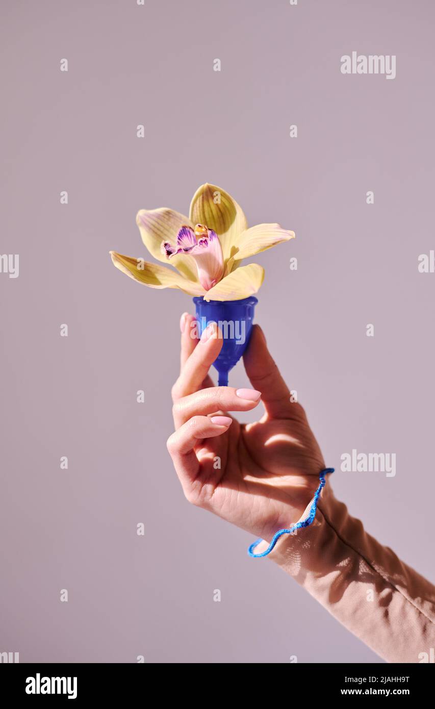 Vertical minimalistic shot of unrecognizable womans hand holding menstrual cup with beautiful flower in it, womens health concept Stock Photo