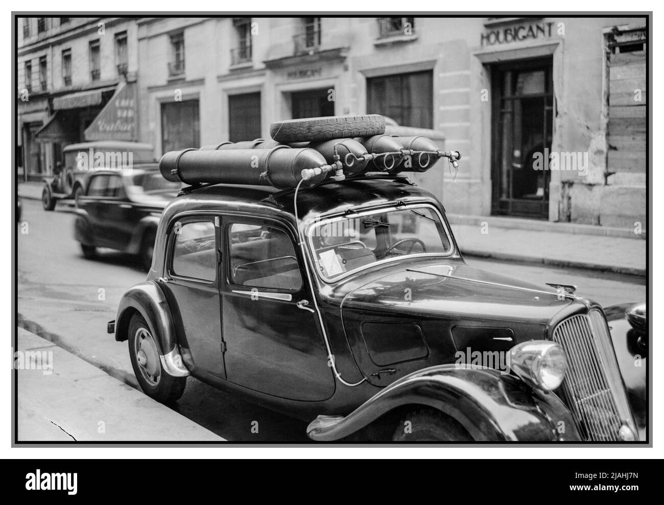 Post War WW2 Car Fuel Gas Bottle alternative.  Rationing France Parisian Traffic, Spring 1945- Everyday Life in post war Paris, France, 1945 A view of a Paris street, showing a car which has been converted to run on gas, rather than petrol which is strictly rationed.. There are four gas cylinders attached to the roof of the car, and a small tube runs downs the side of the car and under the bonnet. Date 1945 Stock Photo