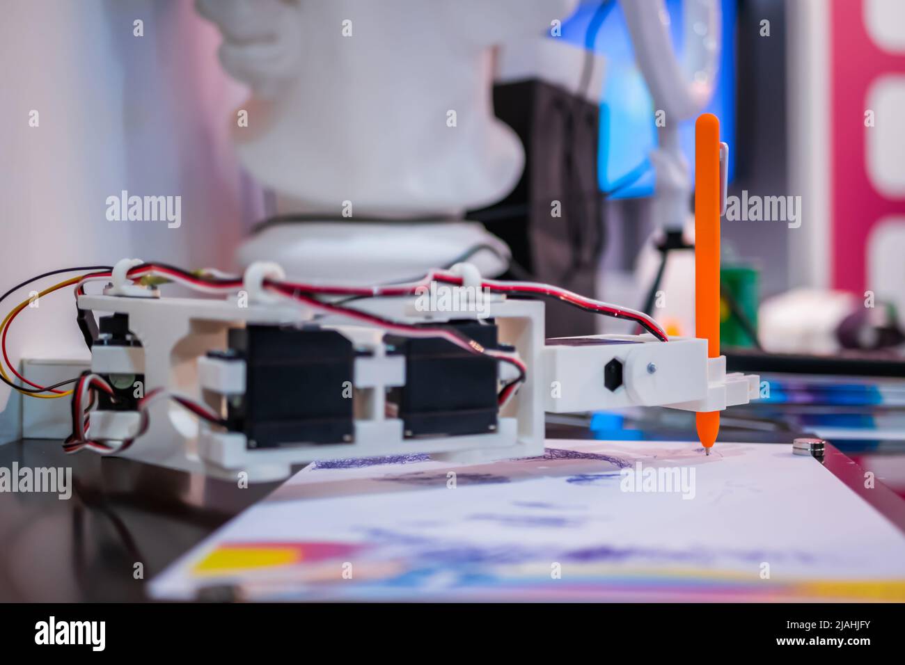 Robotic arm with orange pen drawing portrait at robot futuristic exhibition Stock Photo