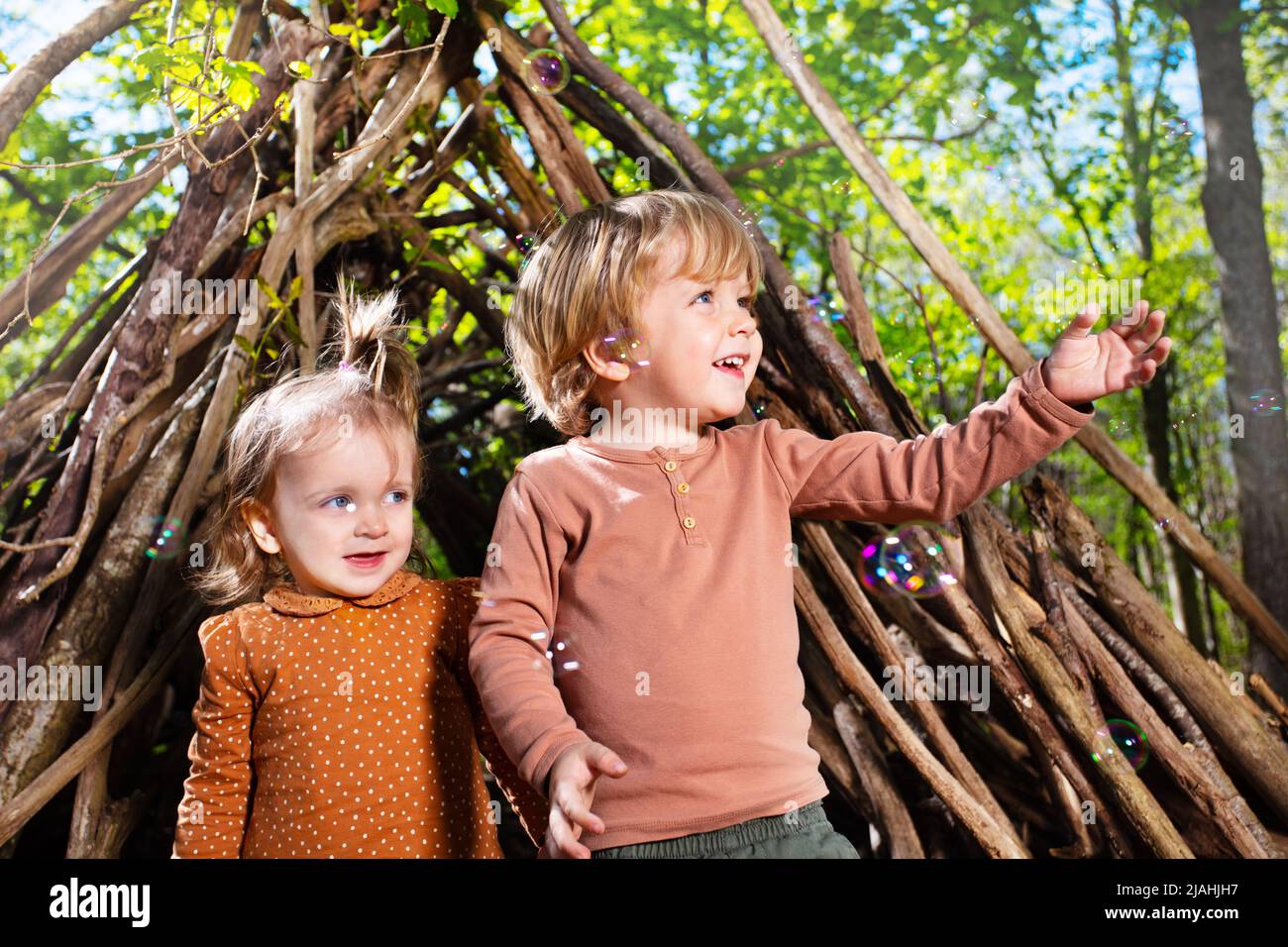 Two children boy, girl play with soap bubbles in hut of branches Stock Photo