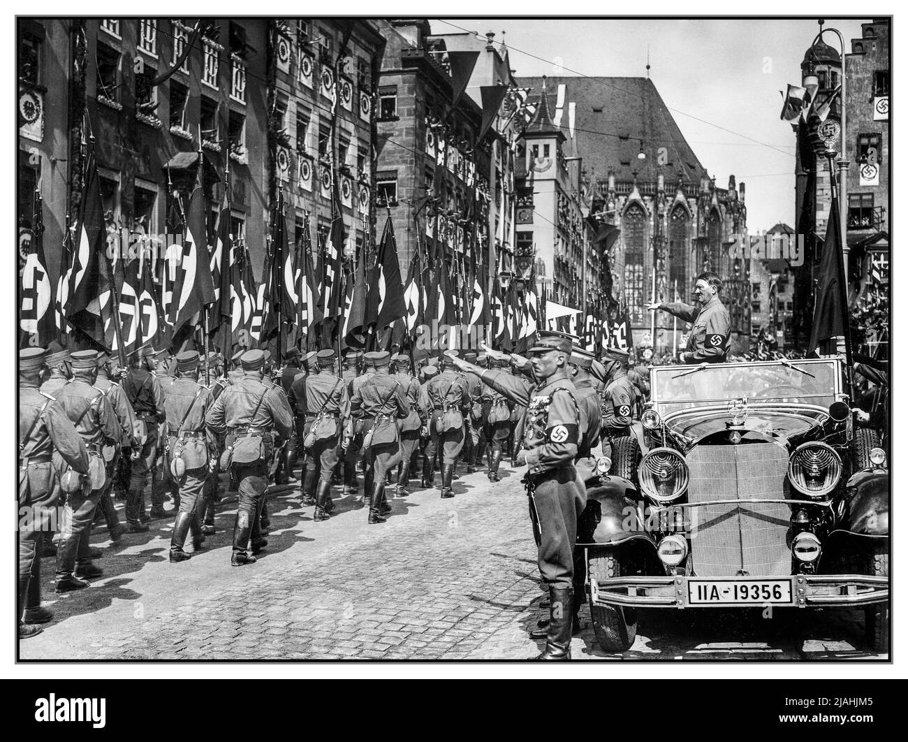 Nuremberg SA Rally 1930s with Adolf Hitler standing in his Mercedes-Benz 770 reviewing SA (Sturmabteilung) members in a parade during the Nuremberg rally 1935, the 7th Nazi Party Congress held in Nuremberg, September 10–16. Hitler is accompanied by the Blutfahne, ('Blood Flag', ceremonial swastika flag) and its bearer SS-Sturmbannführer Jakob Grimminger. Stock Photo