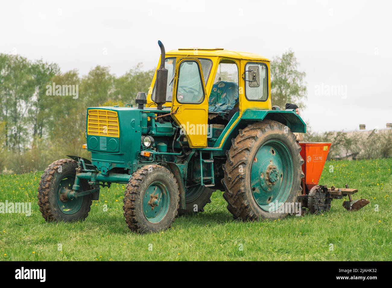 Old farm tractor Belarus on the green grass in an agricultural field in spring ready for the plowing and sowing Stock Photo