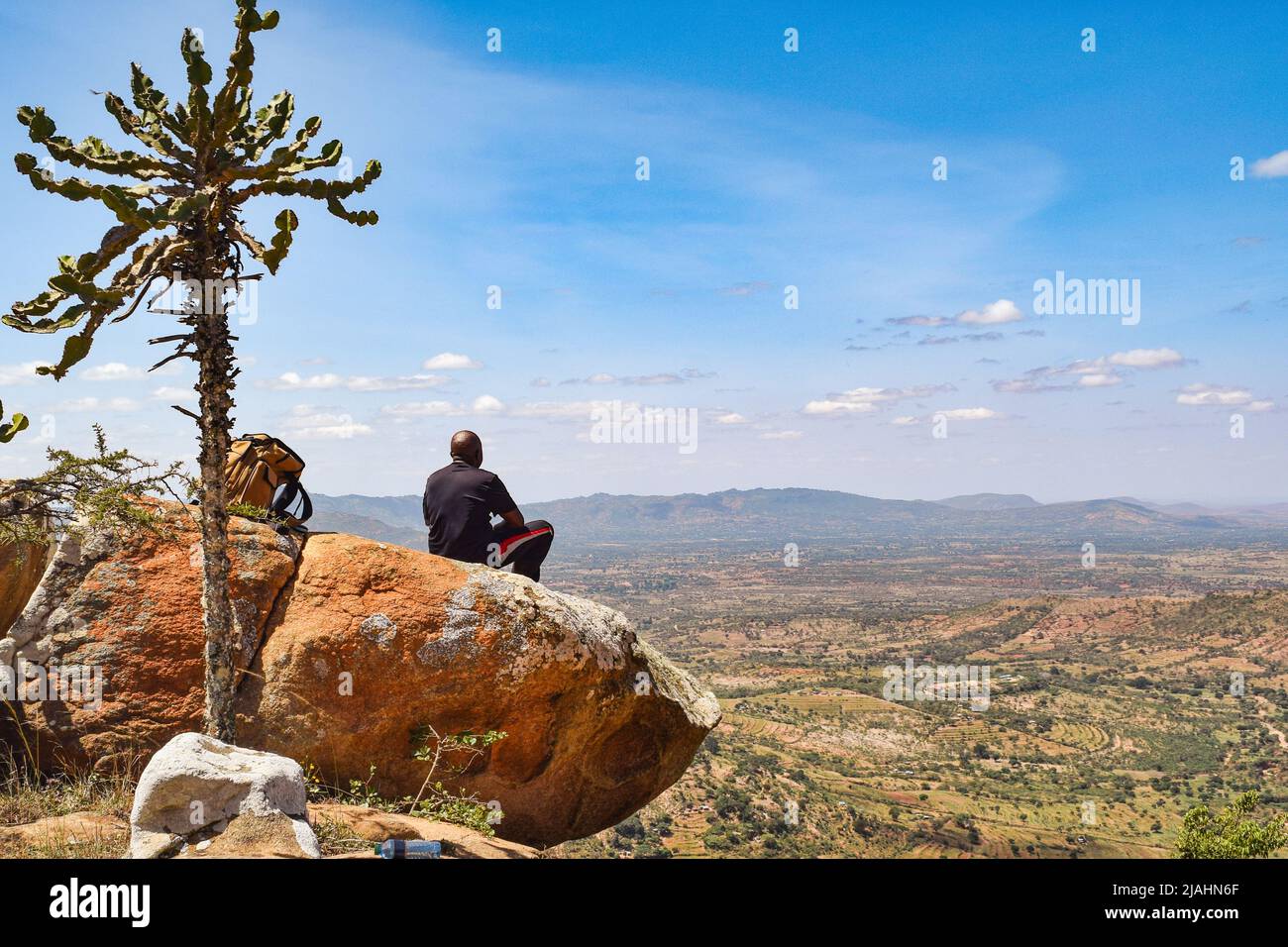 A hiker sitting on a rock at a scenic view point against valley in Makueni, Kenya Stock Photo