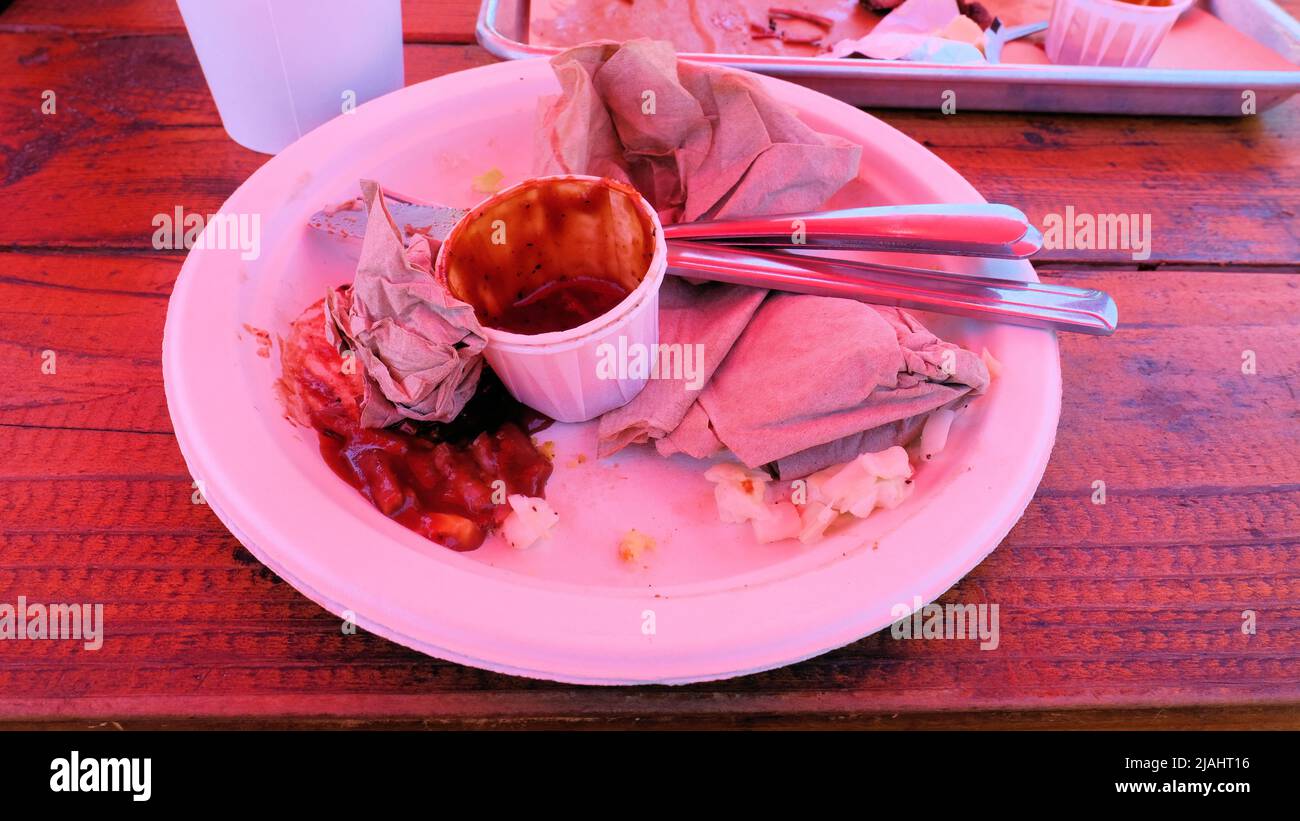 Paper plate with used napkins, cutlery, paper container for barbecue sauce after eating BBQ pork sausage and beef brisket; after dinner leftovers. Stock Photo