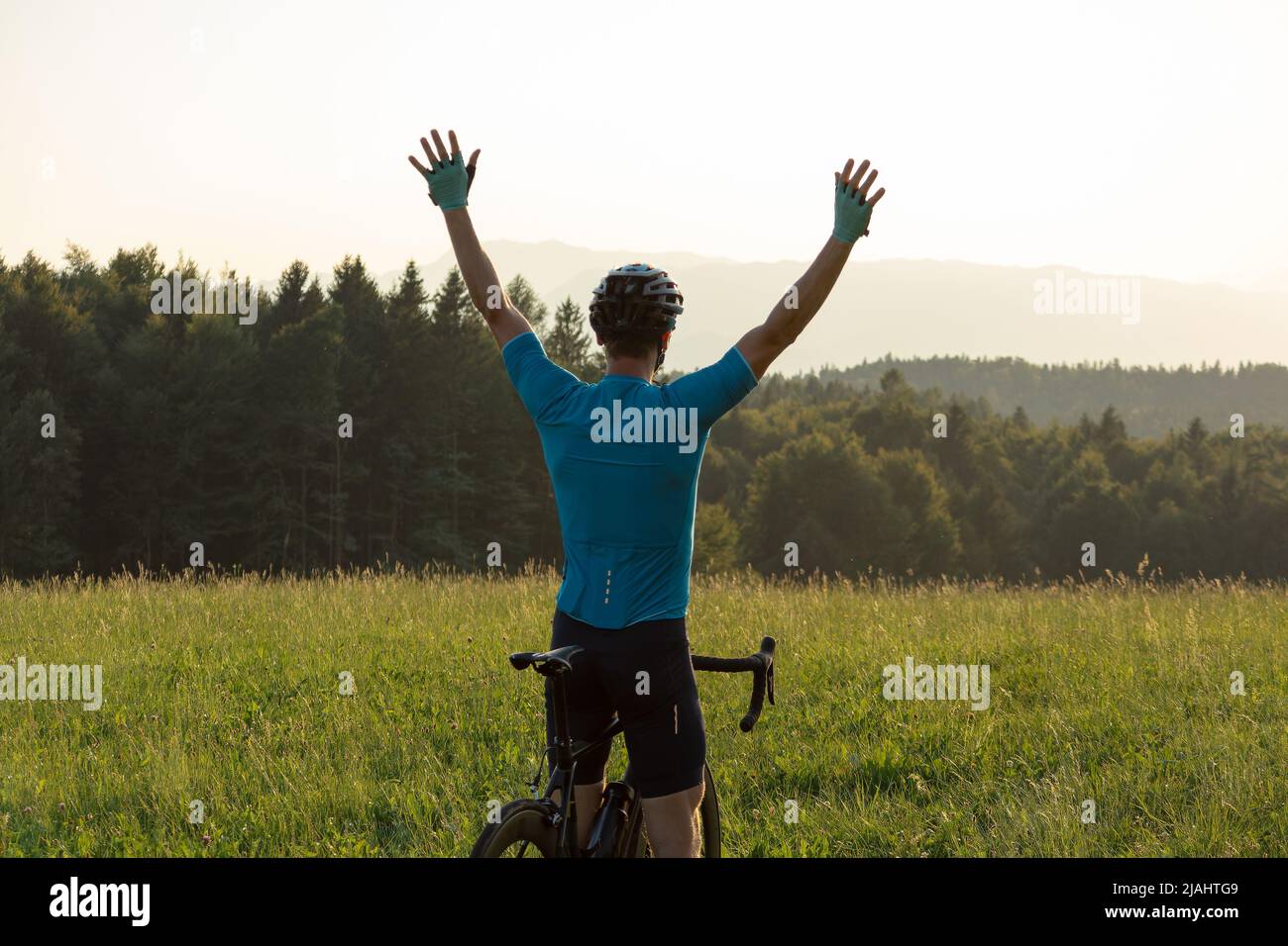 Male athlete professional racing cyclist riding a bike with arms raised ...