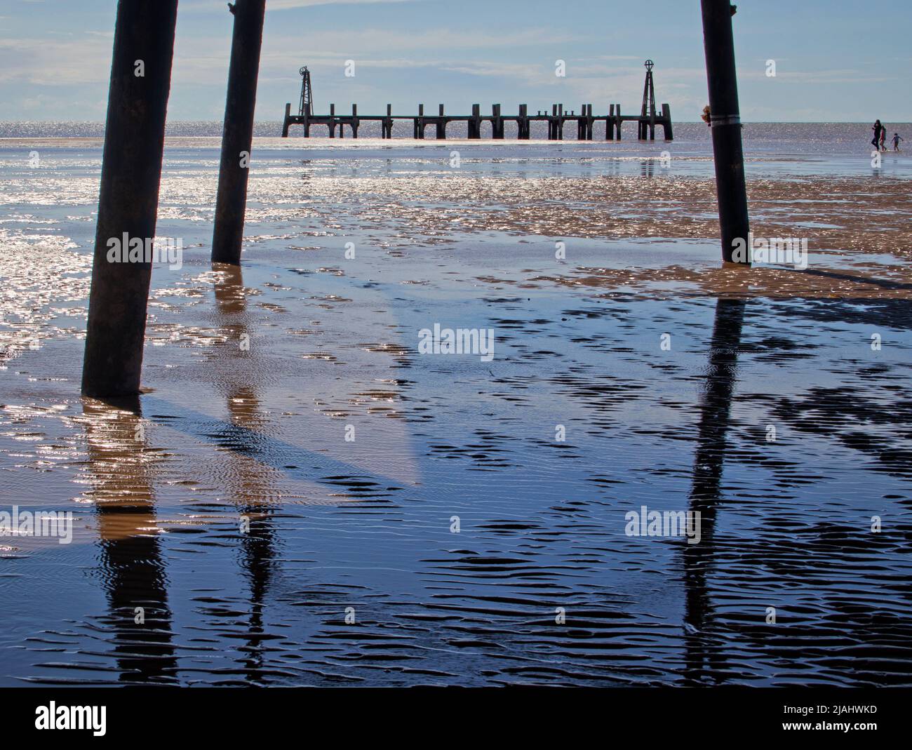 Three distant figures heading for the old pier in St Annes on Sea, viewed through the stanchions of the newer pier Stock Photo