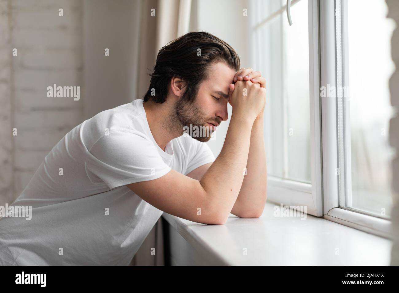 Thoughtful millennial guy standing next to window at home Stock Photo