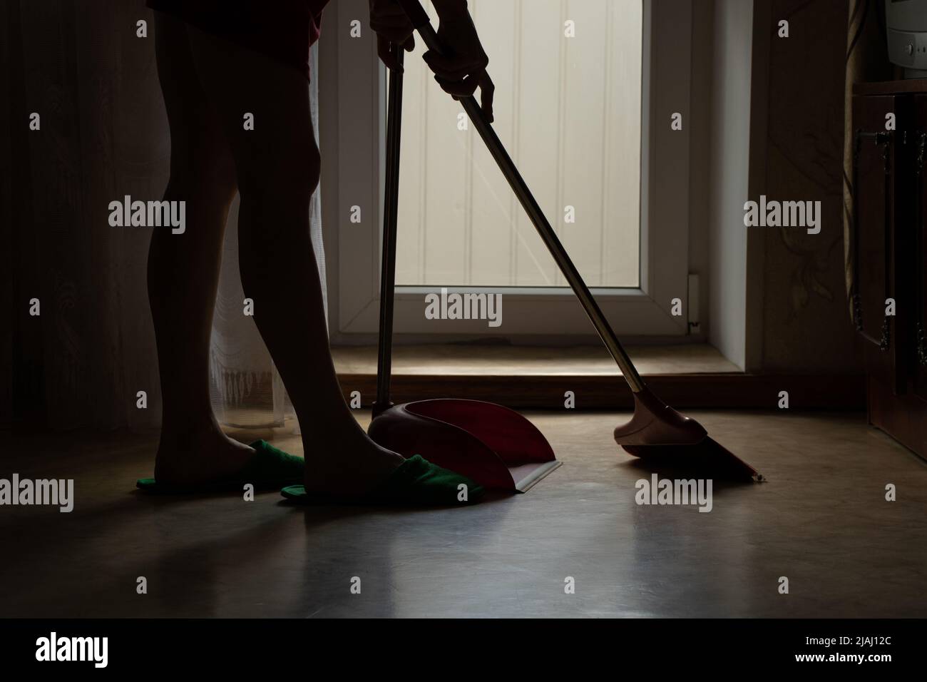 The girl sweeps the floor of the house with a broom and the scoop