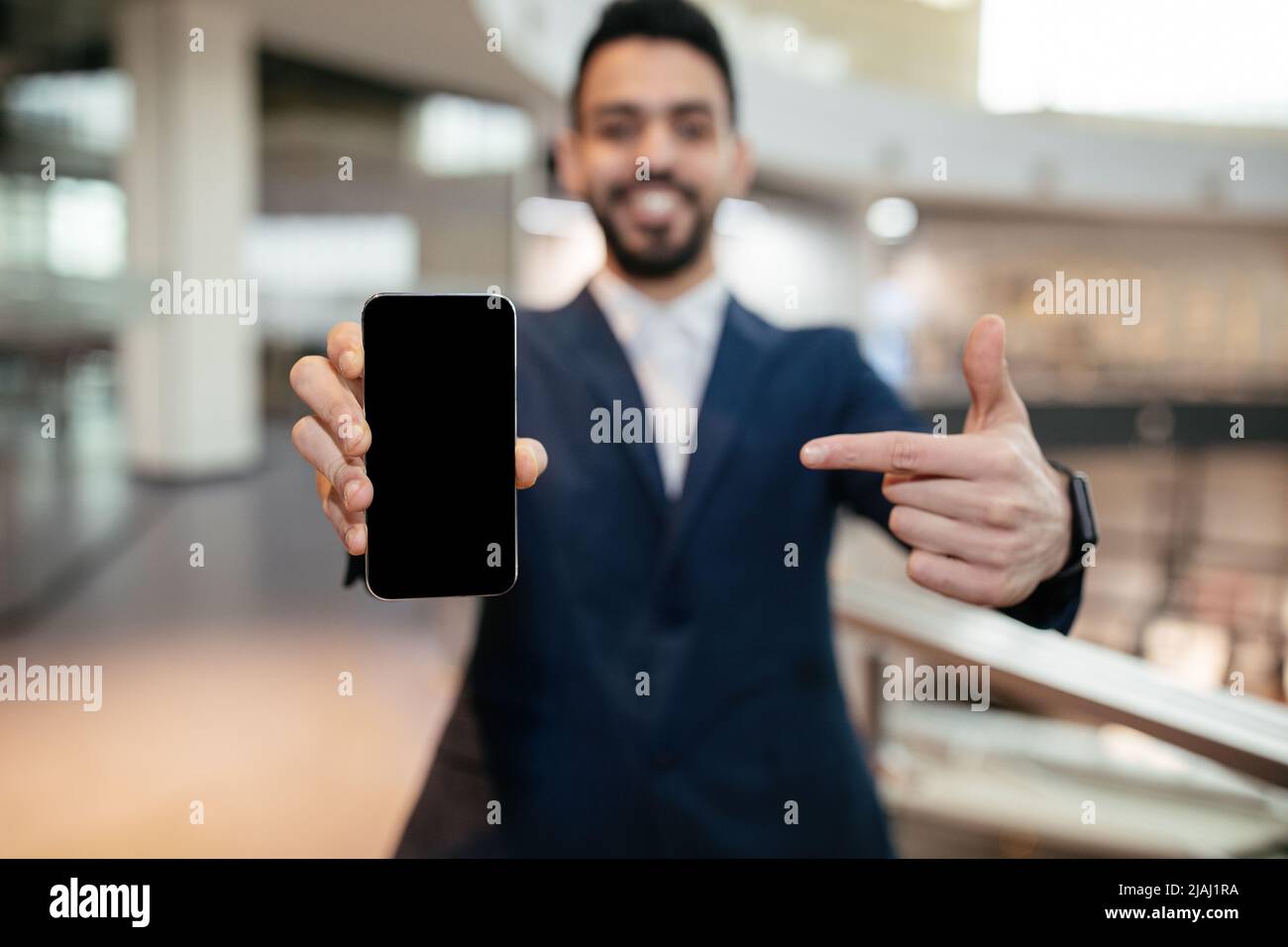 Happy young muslim general manager with beard in suit points finger at phone with empty screen in office Stock Photo
