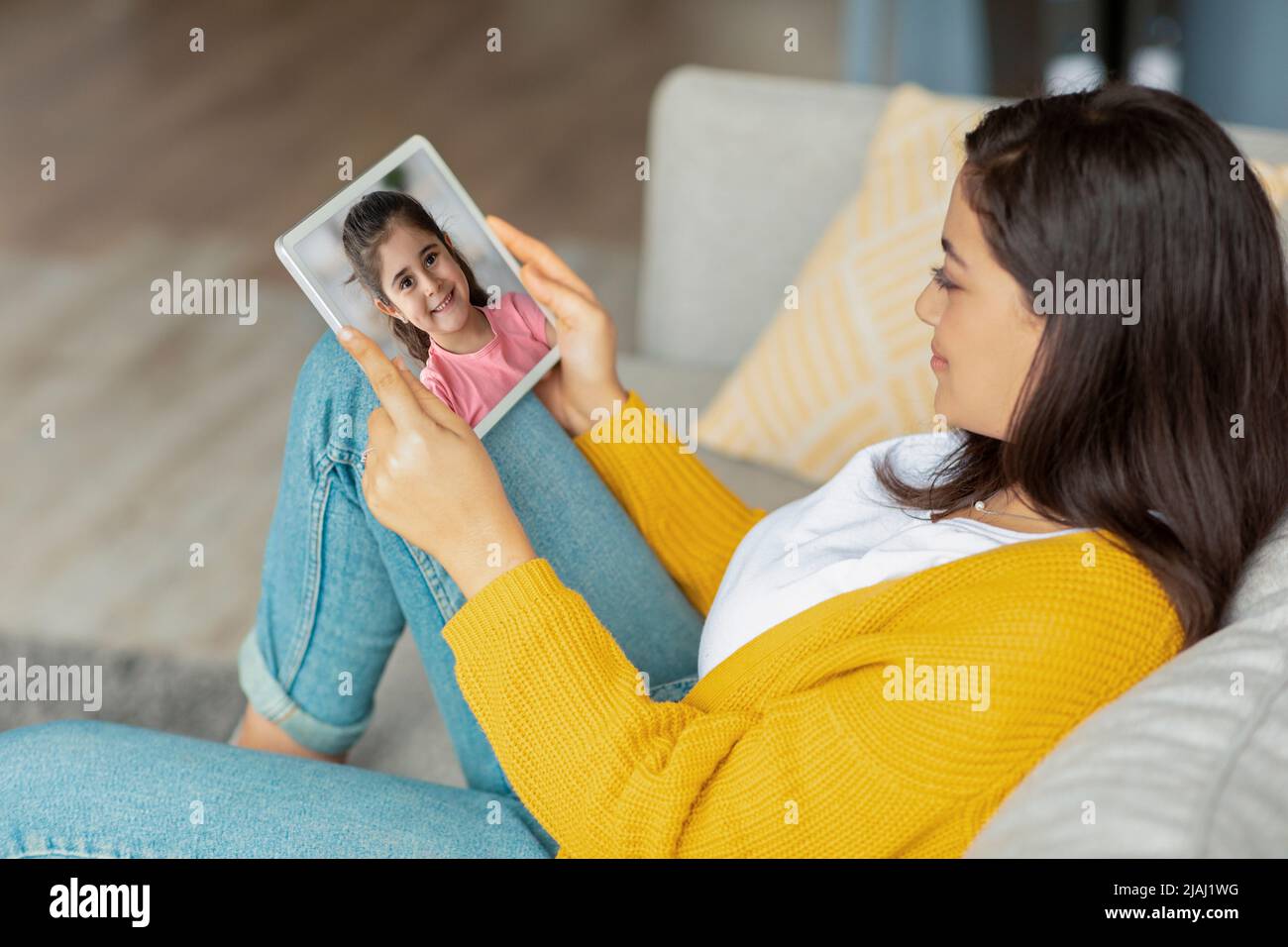 Relaxed middle eastern woman sitting on couch, using tablet Stock Photo