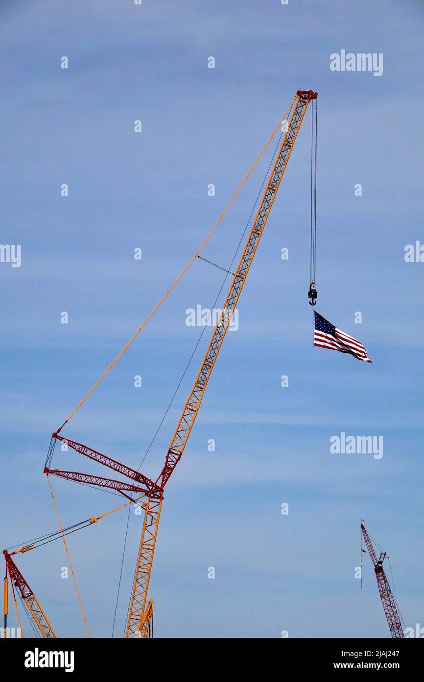 An American flag blows in the wind while being draped from a tall crane on a construction site. Stock Photo