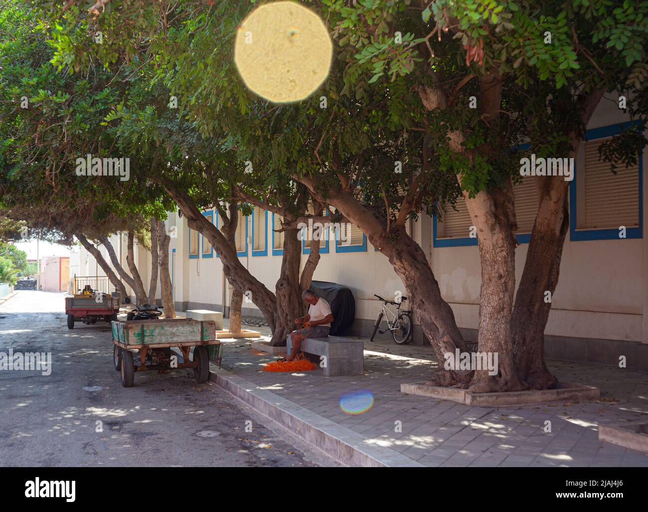 Linosa, Italy - July, 27: An old fisherman sitting on the bench repairing a fishing net on July 27, 2021 Stock Photo