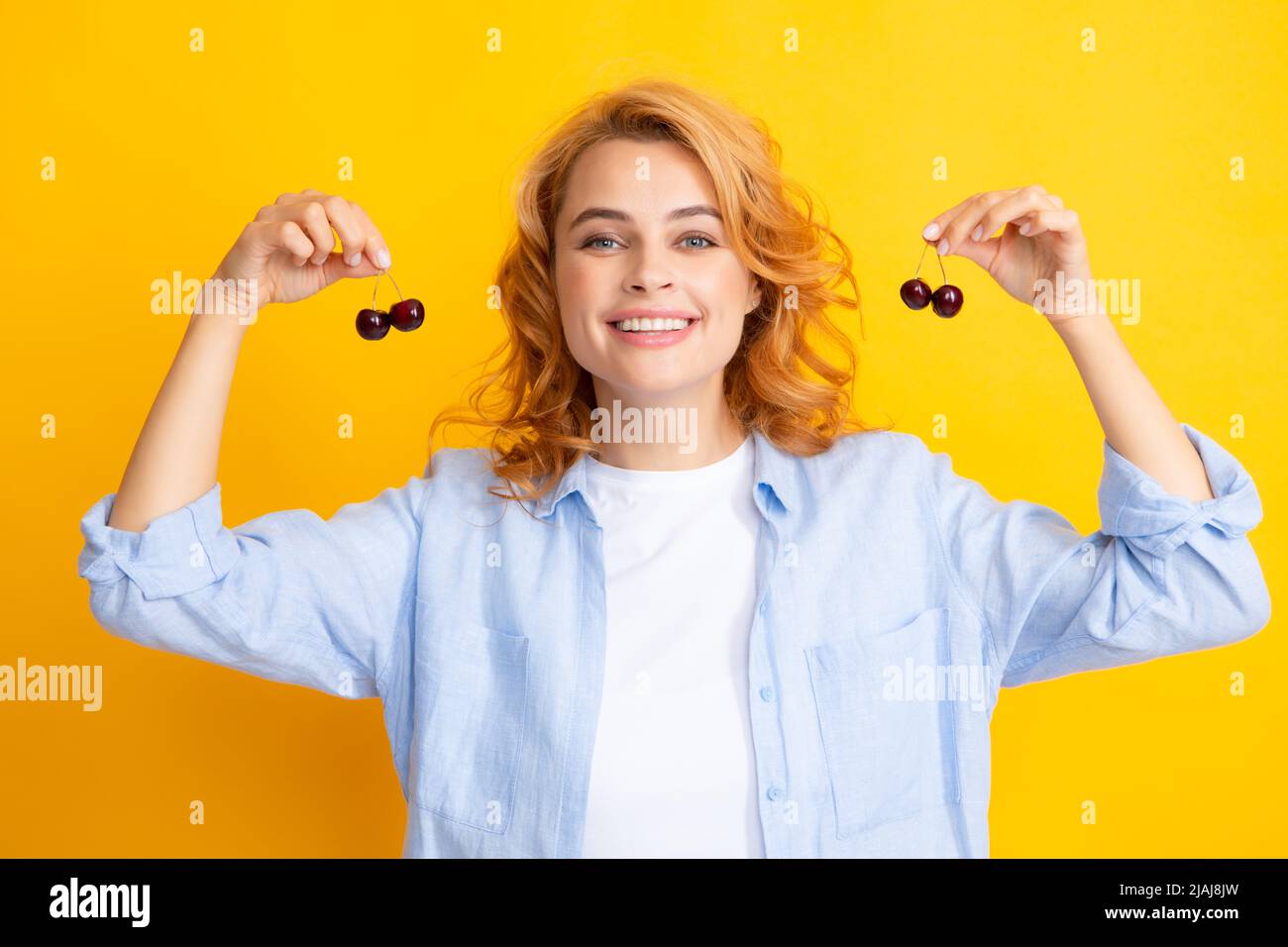 Womans enjoying a fresh sweet cherry. Female eating cherries on yellow background. Stock Photo
