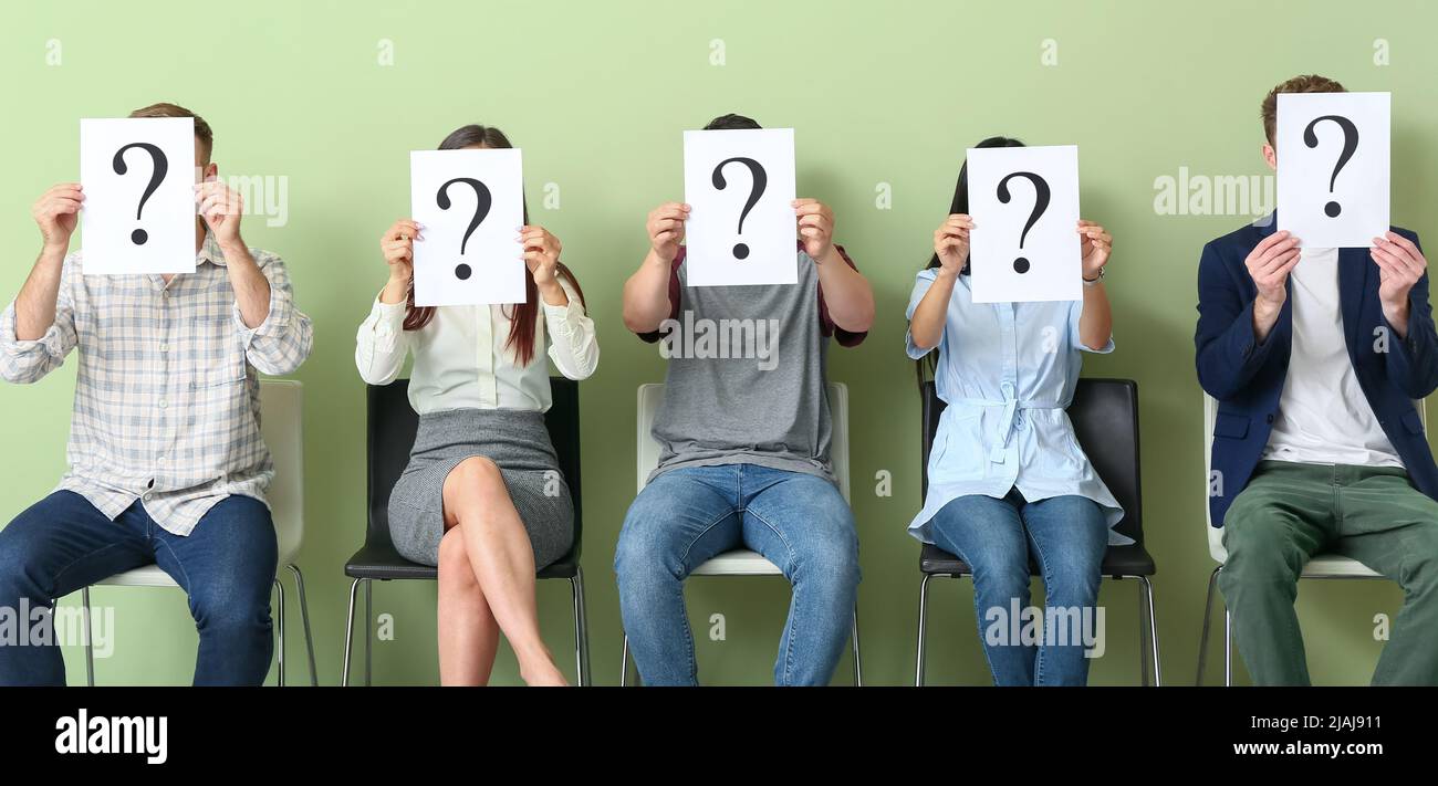 Young people holding paper sheets with question marks while sitting on