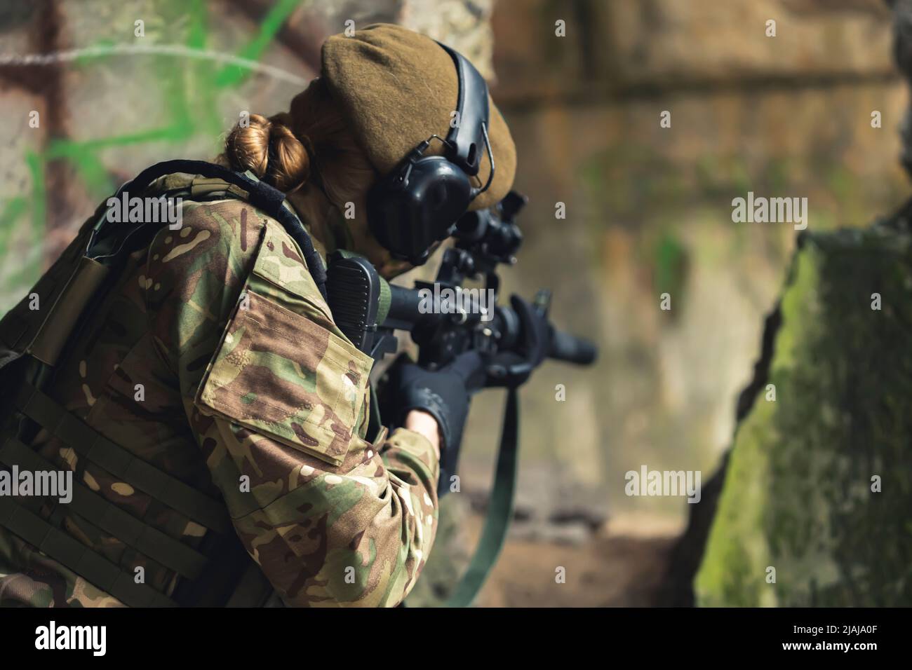 One single servicewoman aiming at target with firearm while wearing camouflage. Outdoor shot from the back. High quality photo Stock Photo
