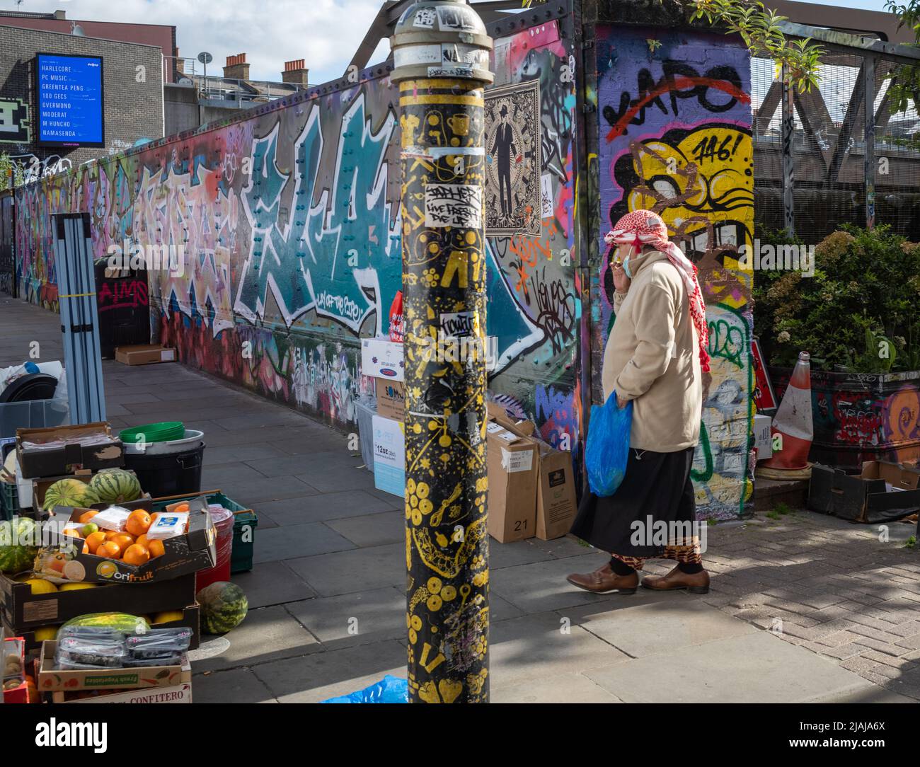 A man dressed in a middle eastern headscarf walks past a fruit stall at Brick Lane Market, London, England, UK Stock Photo