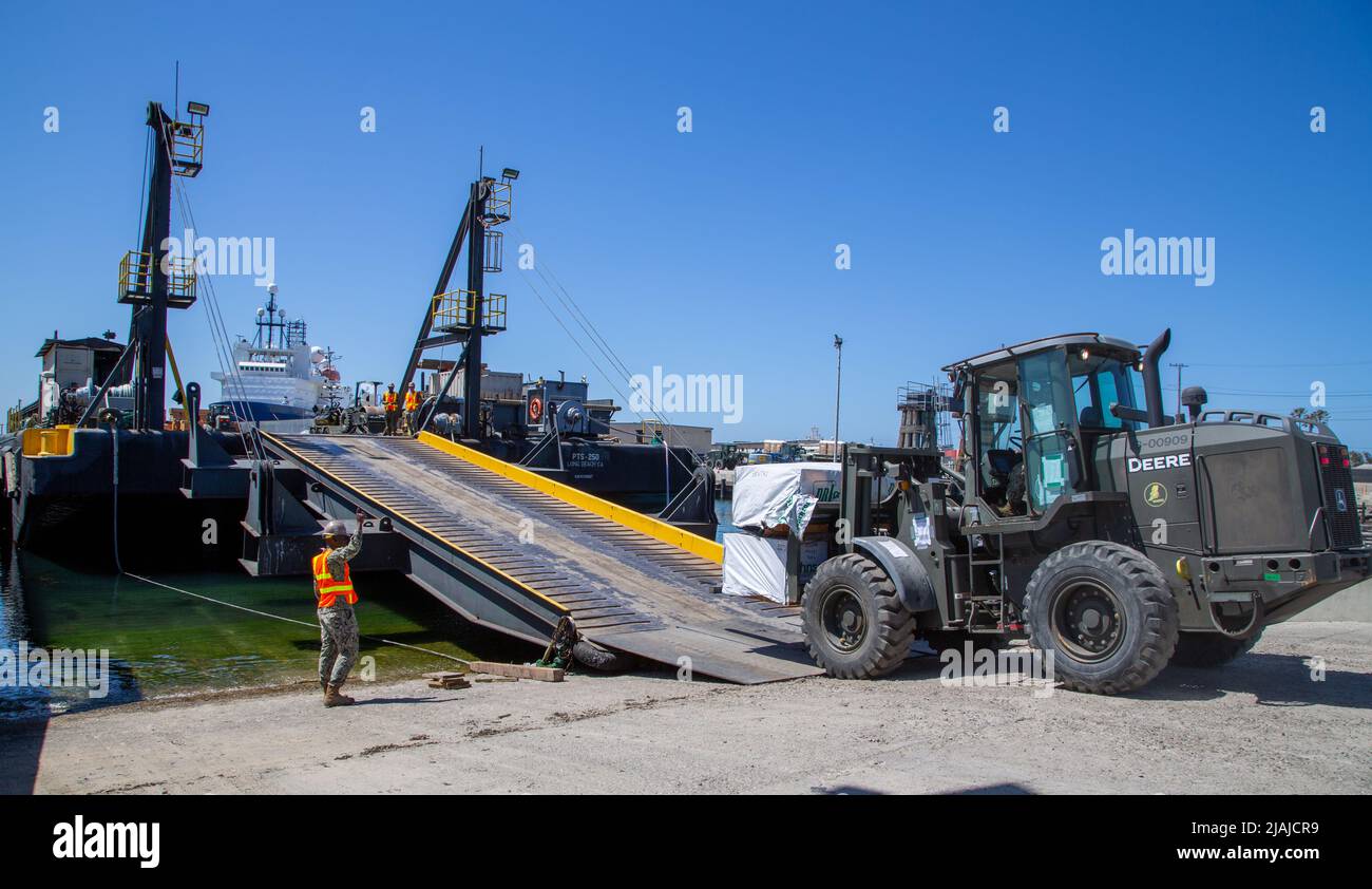 220529-N-PG340-1004 PORT HUENEME, Calif. (May 29, 2022) Construction Mechanic 2nd Class Delroy Belfon, with Naval Mobile Construction Battalion (NMCB) 5, guides the forklift driver onto the deck of a PTS-250 ocean-going landing barge, May 29. The U.S. Navy Seabees with NMCB-5 loaded equipment for Operation Turning Point, also known as their Field Training Exercise. NMCB-5 is homeported out of Port Hueneme. They train on high-quality construction, expeditionary logistics, and combat operations to execute construction and engineering projects for major combat operations, disaster response, and h Stock Photo