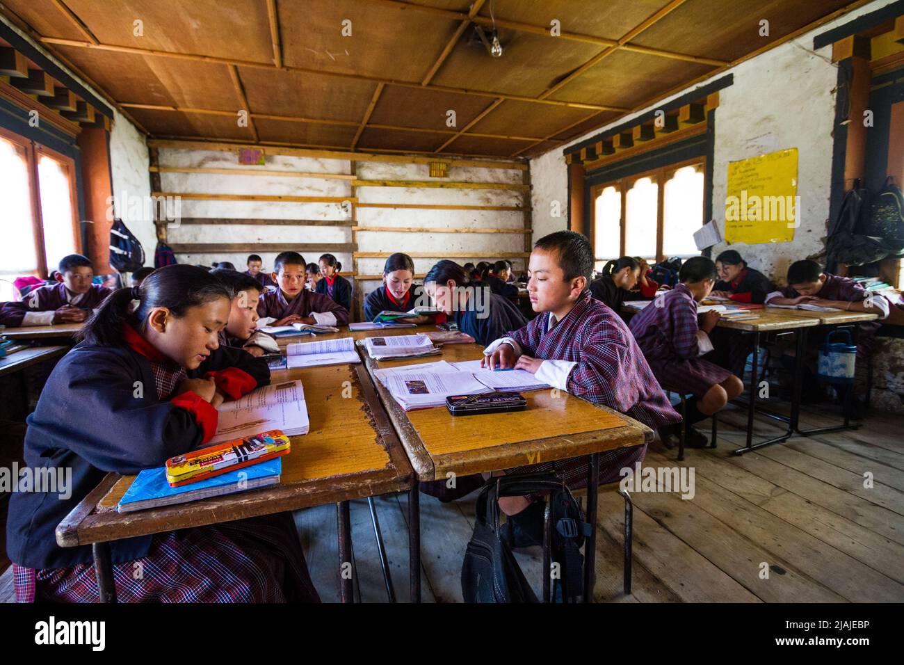 Children are sitting at wooden desks in a rural Bhutan grade school while learning various topics in Bhutan Stock Photo