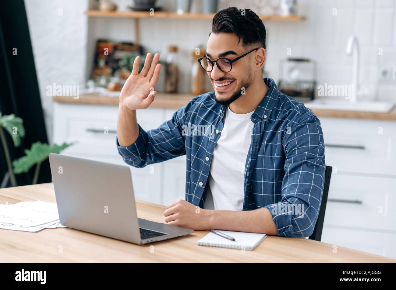 Positive indian or arabian guy, online tutor, freelancer, student, wearing glasses and casual clothes, speaking via video conference, looking at laptop, conducts virtual meeting, work from home,smile Stock Photo