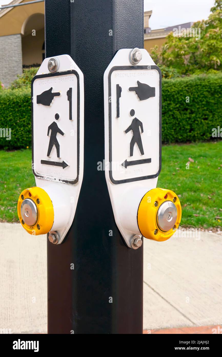 Pedestrian crosswalk button on the corner of two streets indicating direction of crossings. Stock Photo